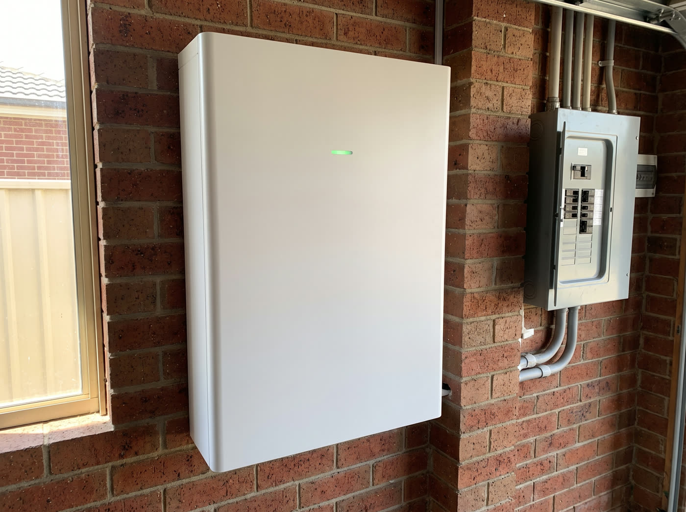 A home battery unit mounted on a brick garage wall